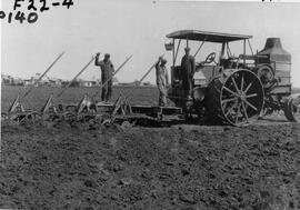 A Tractor drawing four twelve inch plows.